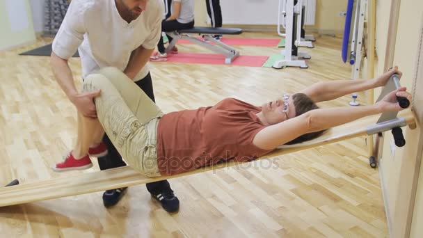 Fisioterapeuta ajudando a mulher idosa a girar as pernas, fazendo exercícios na sala de fitness. Ginástica saudável. Idosos activos . — Vídeo de Stock