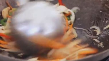 Profesyonel aşçı karıştırma sebze ve mantar bir tavada sokak gıda Festivali'nde yakın çekim.