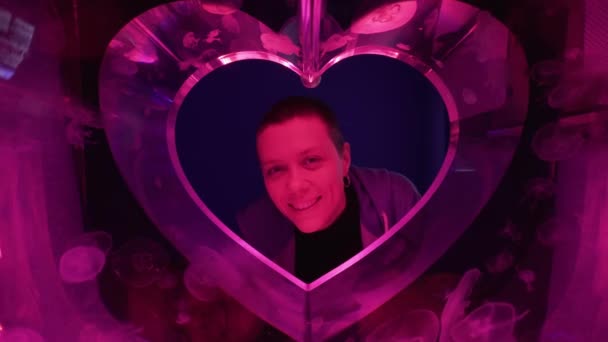 Vrouw glimlachend in abstract hartaquarium gemaakt van kwallen. Roze maankwal of Aurelia Aurita of Schotelgelei. Valentijnsdag concept. — Stockvideo
