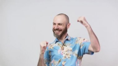 Hawaii gömleği giyen mutlu bir adam beyaz arka plandaki zaferi yavaş çekimde kutluyor. Başarı, zafer, zafer, kazanma ve kutlama duyguları.