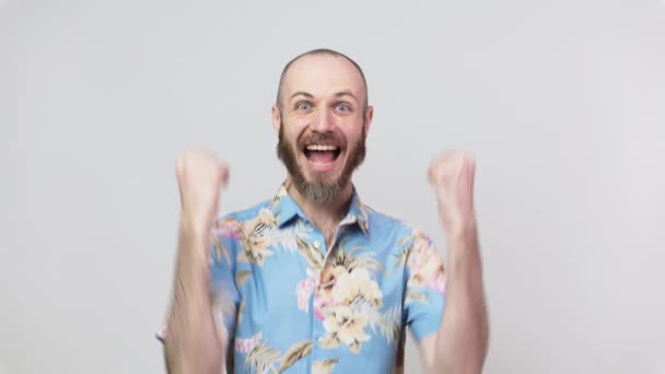 Homem feliz vestindo camisa havaiana celebrando uma vitória sobre o fundo branco. Emoções de sucesso, triunfo, vitória, vitória e celebração . — Vídeo de Stock