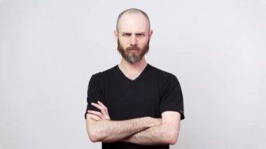 Beyaz arka planda kameraya bakan sert sakallı bir adam. Ciddi tatminsiz adam ellerini çapraz tutar. Duyguların kavramı.