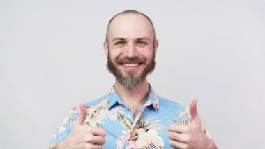 Hawaii gömleği giyen mutlu sakallı adam beyaz arka planda baş parmak gösteriyor. İyi iş, çok iyi. Yavaş Hareket.