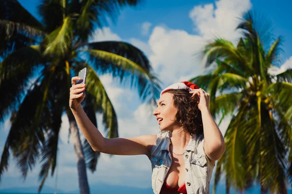 Primer plano de una joven chica sexy delgada en gafas de sol sombrero rojo de Santa Claus en Navidad en Año Nuevo fondo del cielo azul — Foto de Stock