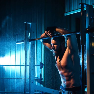 Yakışıklı ve kaslı bir adam, spor salonunda kameraya poz veriyor.