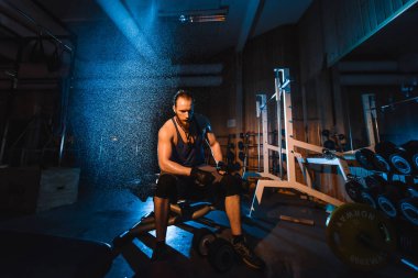 Yakışıklı ve kaslı bir adam, spor salonunda kameraya poz veriyor.