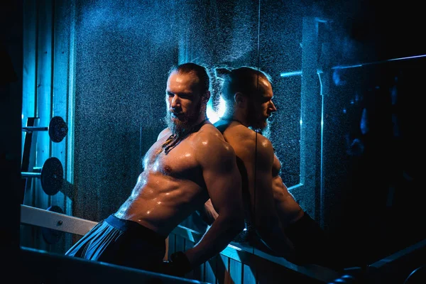 Yakışıklı ve kaslı bir adam, spor salonunda kameraya poz veriyor.