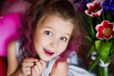 Küçük güzel kız bir gümüş elbisenin içinde kırmızı lale pembe kıvırcık saçlı ve çok renkli topları ile