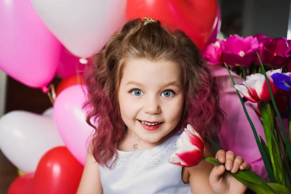 Lilla vackra flicka med rosa lockigt hår i en silver klänning i Röda tulpaner och med flerfärgade bollar — Stockfoto