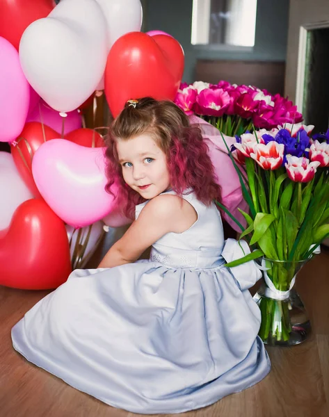 Pequena menina bonita com cabelo encaracolado rosa em um vestido de prata em tulipas vermelhas e com bolas multi-coloridas — Fotografia de Stock