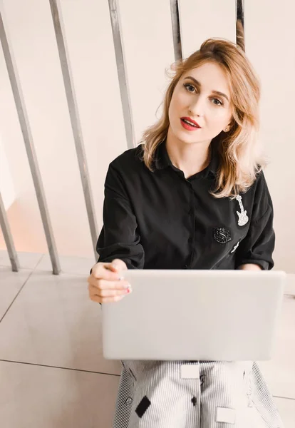 Girl young beautiful blonde hipster with red lips  inside  in black blouse  holds smart laptop tablet using