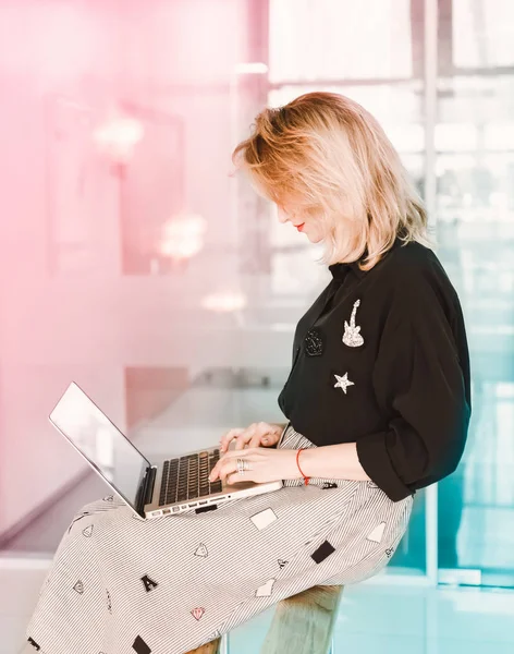 Girl young beautiful blonde hipster with red lips  inside  in black blouse  holds smart laptop tablet using