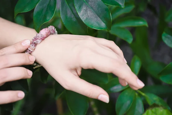 Detail ruky mladé dívky na pozadí zelené tropické listy s přírodními kameny náramek. — Stock fotografie