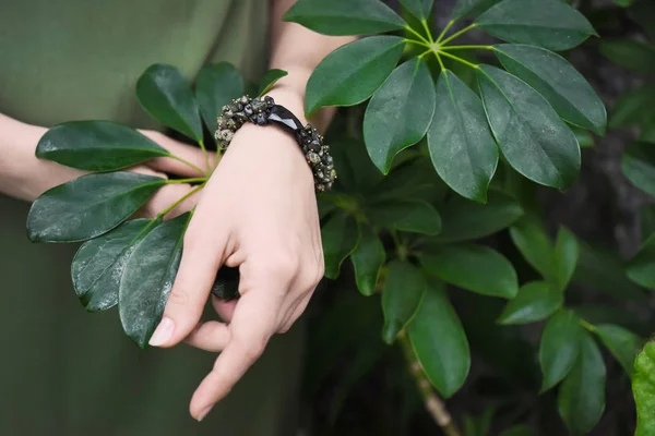 Zbliżenie dłoni młodej dziewczyny na tle zielony tropikalne pozostawia bransoletki wisiorki. — Zdjęcie stockowe