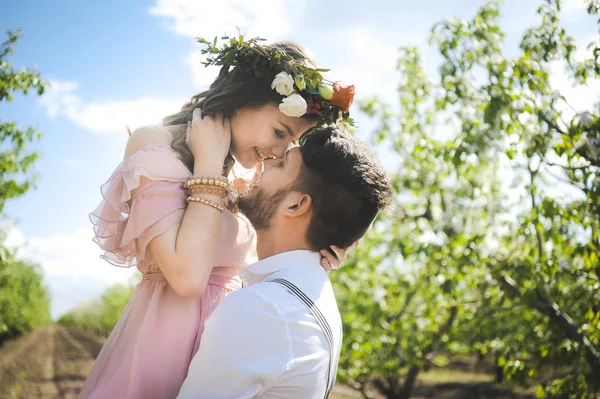 Couple of a girl and  guy looking for a wedding dress, a pink dress flying with a wreath of flowers on her head on a background  garden and the blue sky, and they hug — Stock Photo, Image