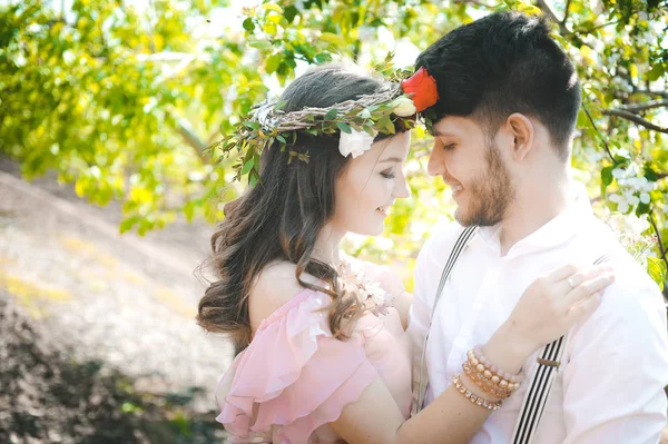 Paar van een meisje en een man op zoek naar een bruiloft jurk, een roze jurk met een krans van bloemen op haar hoofd op een achtergrond tuin en de blauwe lucht, vliegen en ze knuffel — Stockfoto