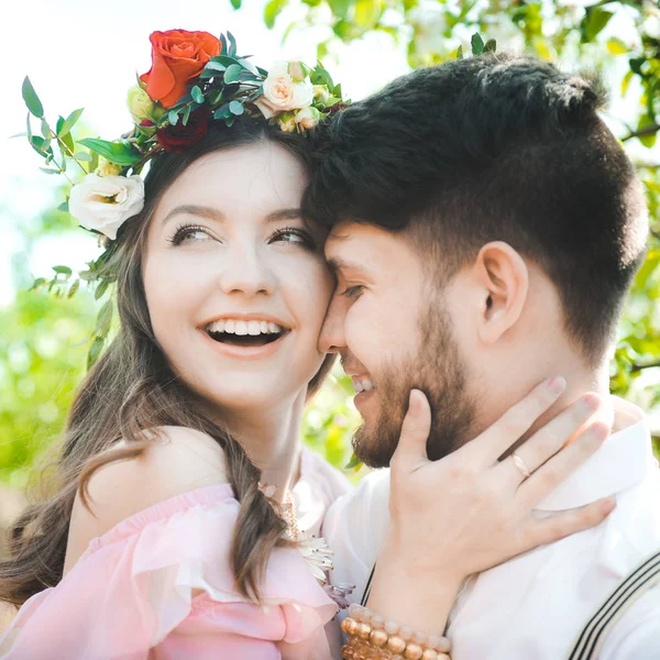少女と男の結婚式をお探しのカップルのドレス、花の花輪と背景庭園、青空の彼女の頭の上飛ぶピンクのドレスと彼らの抱擁 — ストック写真