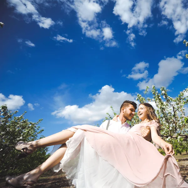 Paar von einem Mädchen und einem Mann auf der Suche nach einem Hochzeitskleid, einem rosa Kleid, das mit einem Blumenkranz auf dem Kopf vor einem Garten im Hintergrund und dem blauen Himmel fliegt, und sie umarmen sich — Stockfoto
