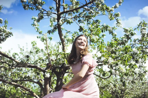 Dziewczyna szuka sukni ślubnej, różowa sukienka latanie z wieniec z kwiatów na głowie na tle ogród i błękitne niebo i przytulić i poza — Zdjęcie stockowe