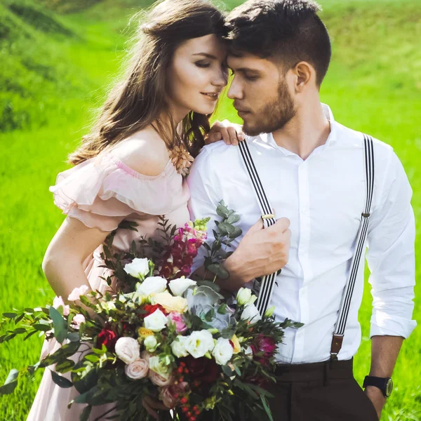 Pareja de una chica y un chico en busca de un vestido de novia, un vestido rosa volando con una corona de flores en la cabeza en un jardín de fondo y el cielo azul, y se abrazan — Foto de Stock