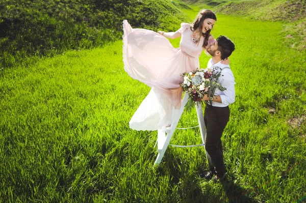 Paar von einem Mädchen und einem Mann auf der Suche nach einem Hochzeitskleid, einem rosa Kleid, das mit einem Blumenkranz auf dem Kopf vor einem Garten im Hintergrund und dem blauen Himmel fliegt, und sie umarmen sich — Stockfoto