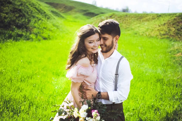 Pareja de una chica y un chico en busca de un vestido de novia, un vestido rosa volando con una corona de flores en la cabeza en un jardín de fondo y el cielo azul, y se abrazan — Foto de Stock