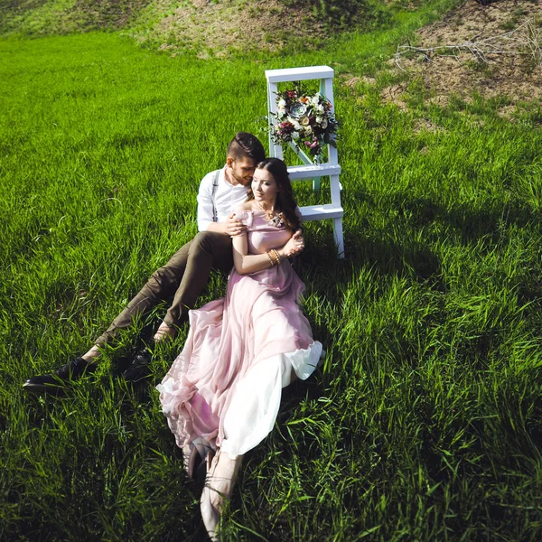 Пара девушка и парень ищет свадебное платье, розовое платье летит с венком цветов на голове на заднем плане сада и голубое небо, и они обнимаются — стоковое фото