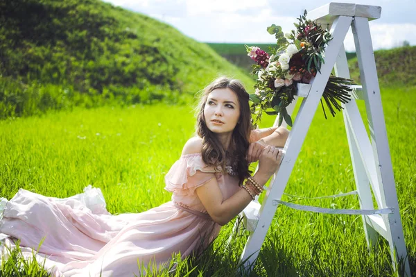 Fille à la recherche d'une robe de mariée, une robe rose volant avec une couronne de fleurs sur la tête sur un jardin d'arrière-plan et le ciel bleu, et ils étreignent et posent — Photo