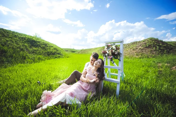 Paar von einem Mädchen und einem Mann auf der Suche nach einem Hochzeitskleid, einem rosa Kleid, das mit einem Blumenkranz auf dem Kopf vor einem Garten im Hintergrund und dem blauen Himmel fliegt, und sie umarmen sich — Stockfoto