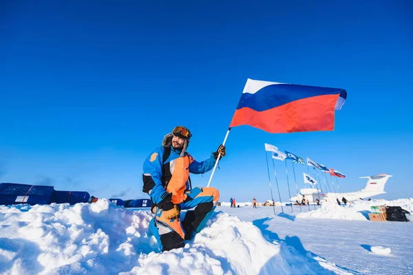 Hombre en una chaqueta de plumón de colores Gorra de piel Barba y bigote en una helada en el fondo del campamento Barneo en un polo norte nevado en el explorador polar de invierno — Foto de Stock