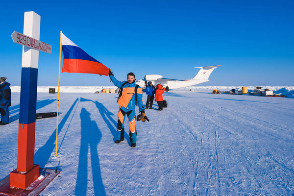 man in a Colorful down jacket Fur cap Beard and mustache in a frost in the background of the camp Barneo on a snowy north pole in winter polar explorer