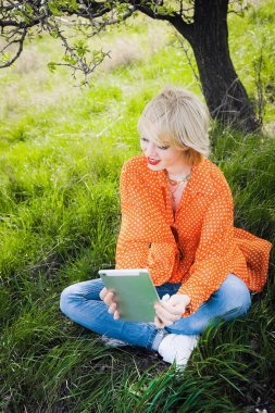 dizüstü bilgisayar ile yeşil çim zemin üzerine kırmızı dolgun dudaklar gülümseyen portre açık havada genç kız güzel bir turuncu hipster sarışın parlak neşeli nokta bluz