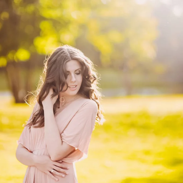 Όμορφη ελκυστική γυναίκα του μια νεαρή κοπέλα λεπτή μελαχρινή με μακρύ φόρεμα περπατώντας μέσα από ένα καταπράσινο πάρκο με λουλούδια στο ηλιοβασίλεμα στον τρόπο ζωής — Φωτογραφία Αρχείου