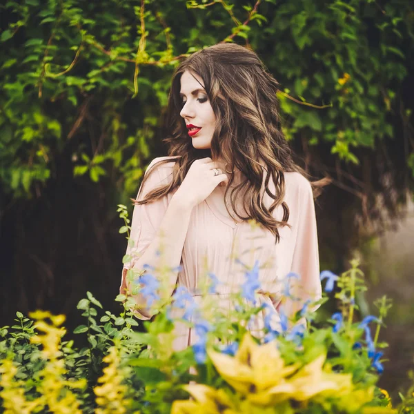 Belle dame attrayante d'une jeune fille brune mince avec robe longue marchant dans un parc verdoyant avec des fleurs au coucher du soleil style de vie — Photo