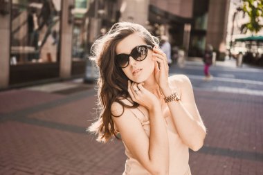 güzel bir ince genç kız blogger portresi şehir merkezinde esmer dusseldorf pastel elbise ve bir Bayan yürüyüş pozlar ve günbatımı üzerinde gülümseyen güneş gözlüğü takıyor
