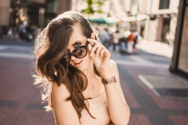 güzel bir ince genç kız blogger portresi şehir merkezinde esmer dusseldorf pastel elbise ve bir Bayan yürüyüş pozlar ve günbatımı üzerinde gülümseyen güneş gözlüğü takıyor