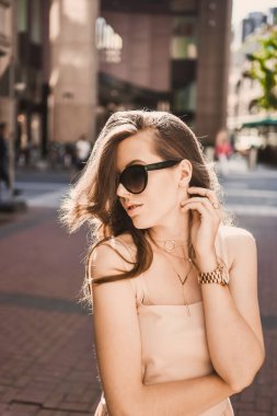 güzel bir ince genç kız blogger portresi şehir merkezinde esmer dusseldorf pastel elbise ve bir Bayan yürüyüş pozlar ve günbatımı üzerinde gülümseyen güneş gözlüğü takıyor