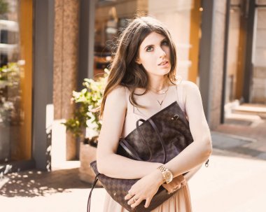 güzel bir ince genç kız blogger portresi şehir merkezinde esmer dusseldorf pastel elbise ve bir Bayan yürüyüş pozlar ve günbatımı üzerinde gülümseyen güneş gözlüğü takıyor