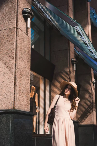 Portrait of a slender young girl blogger beautiful brunette in downtown dusseldorf in a pastel dress and a lady's hat wearing sunglasses walking poses and smiling on the sunset — Stock Photo, Image