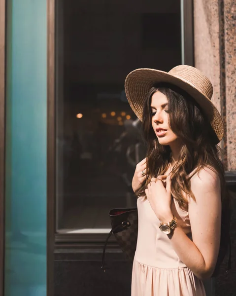 Retrato de una delgada joven blogger hermosa morena en el centro de Dusseldorf con un vestido de pastel y un sombrero de señora con gafas de sol caminando poses y sonriendo en la puesta de sol — Foto de Stock