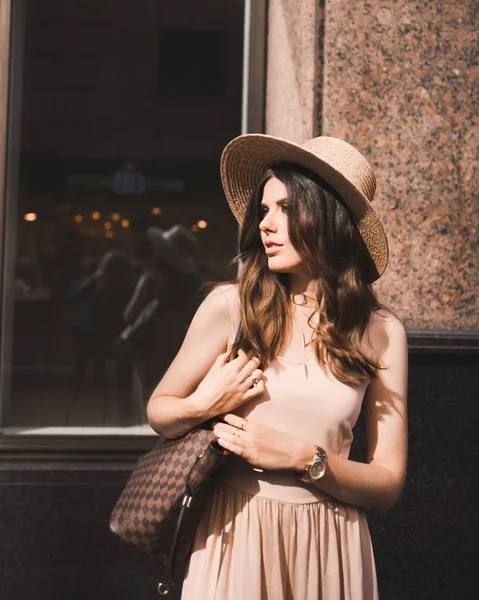 Porträt einer schlanken jungen Bloggerin schöne Brünette in der Innenstadt von Düsseldorf in einem pastellfarbenen Kleid und einem Damenhut mit Sonnenbrille zu Fuß posiert und lächelt auf den Sonnenuntergang — Stockfoto