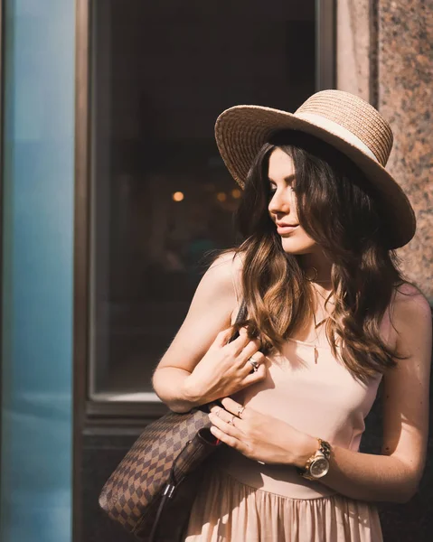 Retrato de una delgada joven blogger hermosa morena en el centro de Dusseldorf con un vestido de pastel y un sombrero de señora con gafas de sol caminando poses y sonriendo en la puesta de sol — Foto de Stock