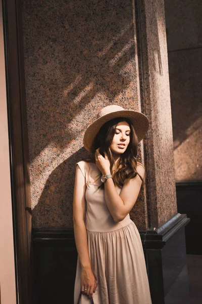 Portrait of a slender young girl blogger beautiful brunette in downtown dusseldorf in a pastel dress and a lady's hat wearing sunglasses walking poses and smiling on the sunset — Stock Photo, Image