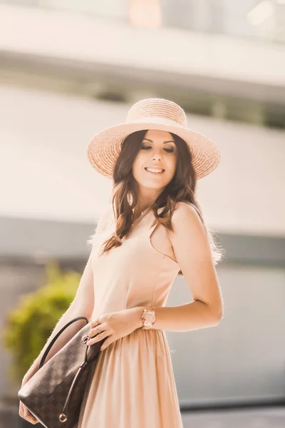 Retrato de una delgada joven blogger hermosa morena en el centro de Dusseldorf con un vestido de pastel y un sombrero de señora con gafas de sol caminando poses y sonriendo en la puesta de sol — Foto de Stock