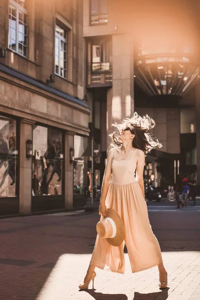 güzel bir ince genç kız blogger portresi şehir merkezinde esmer dusseldorf pastel elbise ve bir Bayan yürüyüş pozlar ve günbatımı üzerinde gülümseyen güneş gözlüğü takıyor