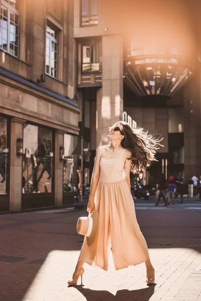 Portrait of a slender young girl blogger beautiful brunette in downtown dusseldorf in a pastel dress and a lady wearing sunglasses walking poses and smiling on the sunset — Stock Photo, Image