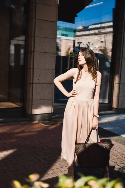 Porträt einer schlanken jungen Bloggerin schöne Brünette in der Düsseldorfer Innenstadt in einem pastellfarbenen Kleid und einer Dame mit Sonnenbrille, die im Sonnenuntergang posiert und lächelt — Stockfoto