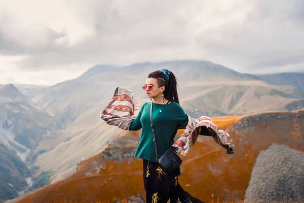 Портрет молодой красивой хипстерки в солнцезащитных очках с дредом в одежде цыганского хиппи на фоне облачного неба и осенних гор Грузии танцующих — стоковое фото