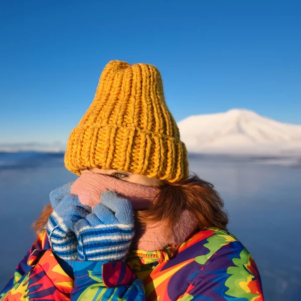 一个女孩的特写在彩虹羽绒服黄色针织帽与红色头发美丽的年轻头发在山的背景下朗伊尔城挪威天北极冬季 — 图库照片