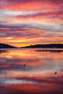 Gün batımının güzel portakal rengi günbatımı manzarası. Norveç 'in Tonsberg şehrinin yakınlarındaki fiyortta pembe bulutların yansıması. Karlı evlerde kırağı var.